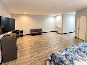 Een moderne hotelkamer met een flatscreen televisie, een bank, een kleine kitchenette en een bed met een geborduurd sprei.