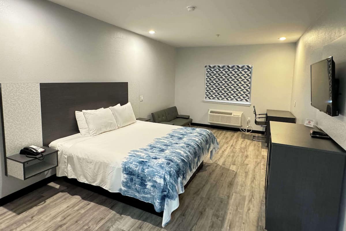 Een moderne hotelkamer met een groot bed, nachtkastje met telefoon, bureau met stoel, televisie en een kamerblind met patroon.
