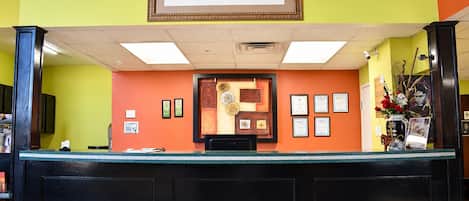 A reception desk with a framed certificate display, a clock, and a vase with flowers.