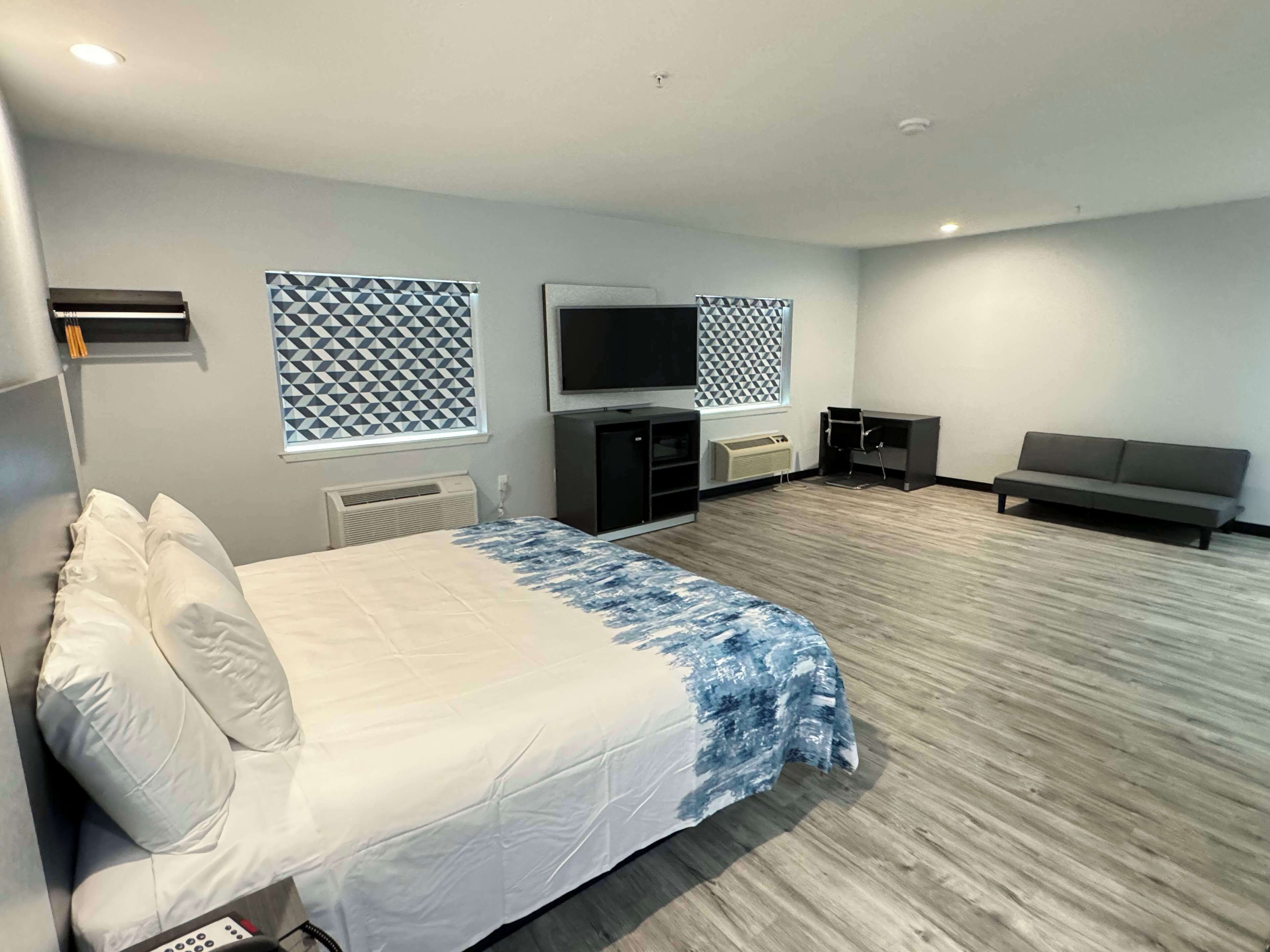 A modern hotel room with a large bed, a TV, a sofa, and a desk.