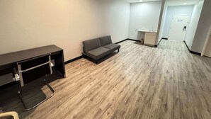 A modern living room with a grey sofa, a black desk, and a wooden floor. - Americas Best Value Inn & Suites Haltom City Ft. Worth (Haltom City)