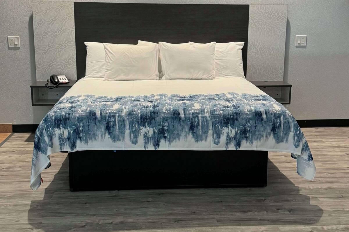 Een moderne hotelkamer met een groot bed, een donker hoofdeinde en een nachtkastje met een telefoon.