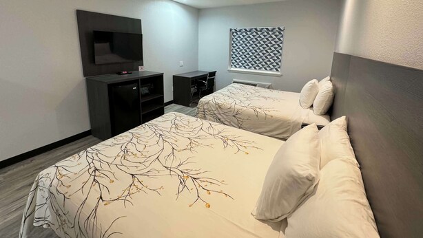 A modern hotel room with two beds, a TV, a desk, and a window with a geometric pattern. - Americas Best Value Inn & Suites Haltom City Ft. Worth (Haltom City)