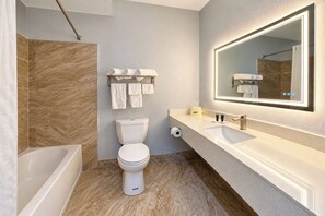 Een moderne badkamer met een badkuip, toilet en wastafel met een grote spiegel.