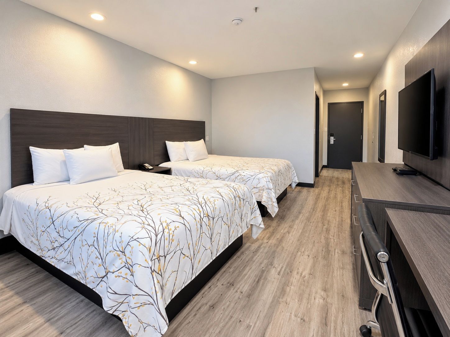A hotel room with two beds, a desk, and a TV.