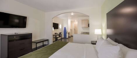 Habitación de hotel con cama, escritorio, silla, televisión y baño visible a través de un arco.