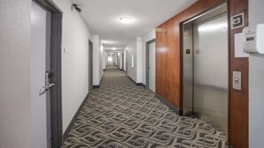 A hotel hallway with carpeted floors, wooden doors, and an elevator. - Quality Inn & Suites Clayton, NM (Clayton)