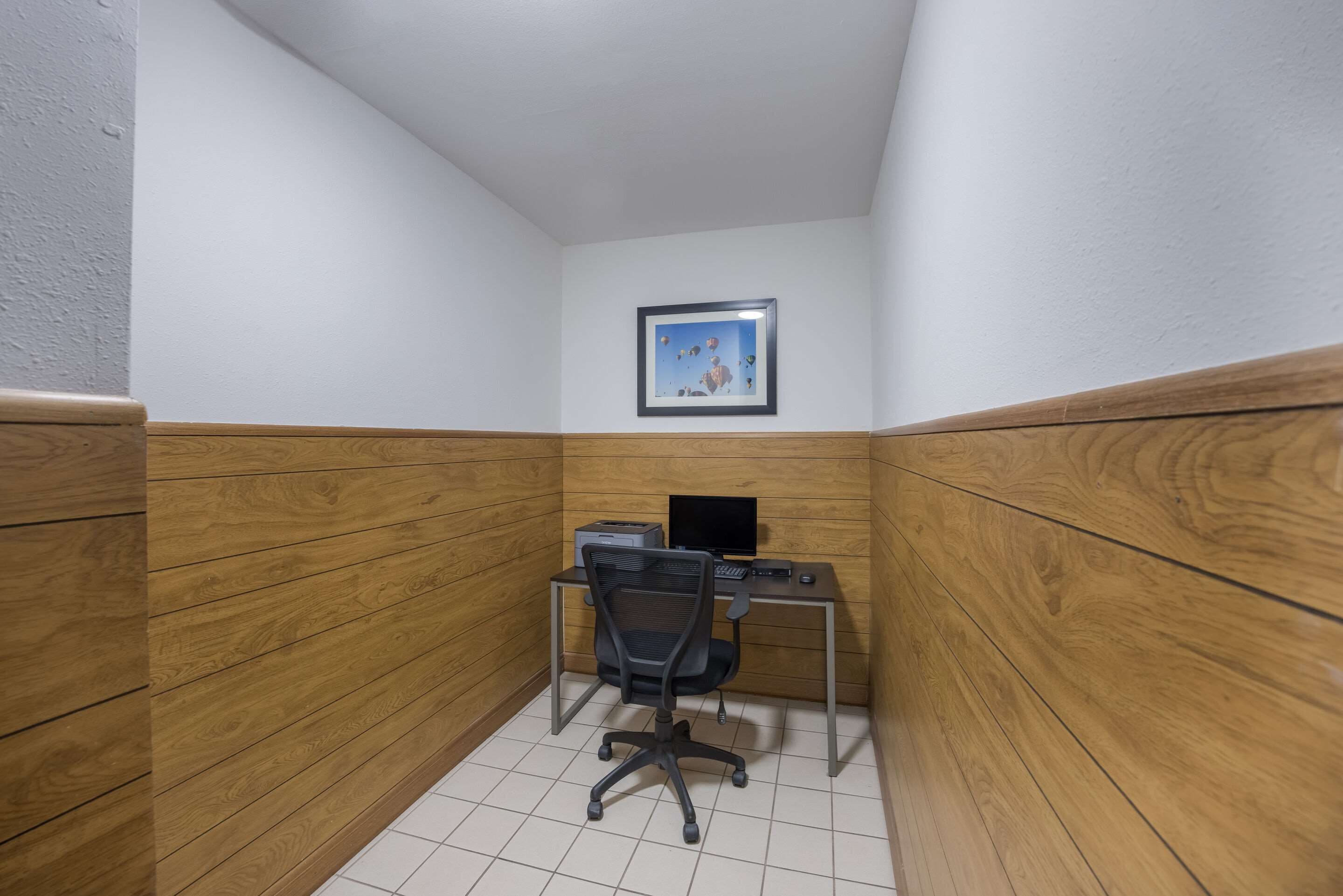A small office space with a wooden desk, a black office chair, and a framed picture on the wall.