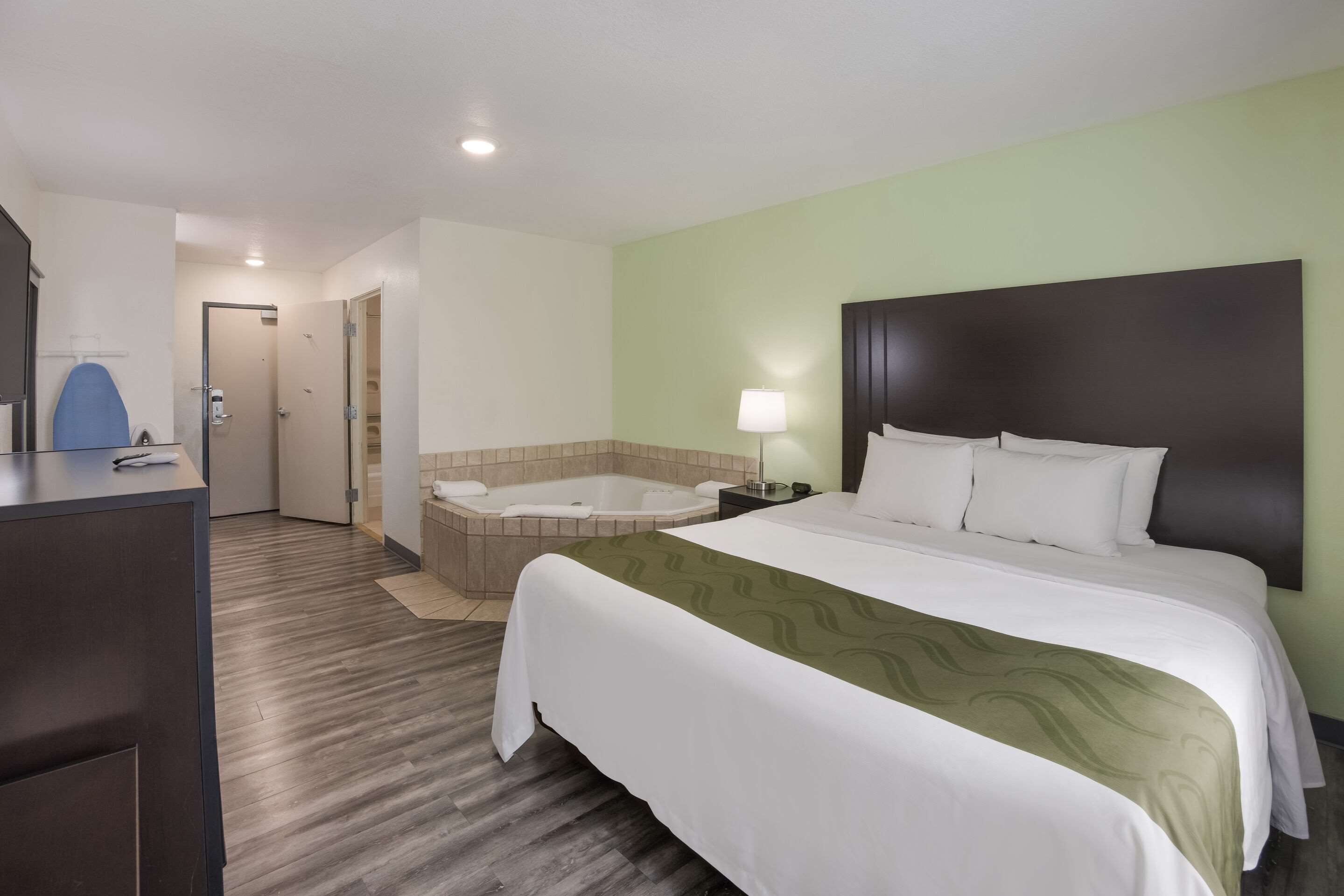 A hotel room with a large bed, a separate bathroom with a bathtub, and a desk with a lamp.