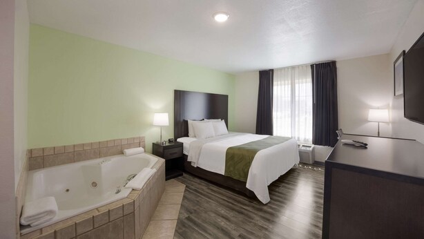 A hotel room with a large bed, a separate bathroom with a bathtub, a desk, and a TV. - Quality Inn & Suites Clayton, NM (Clayton)