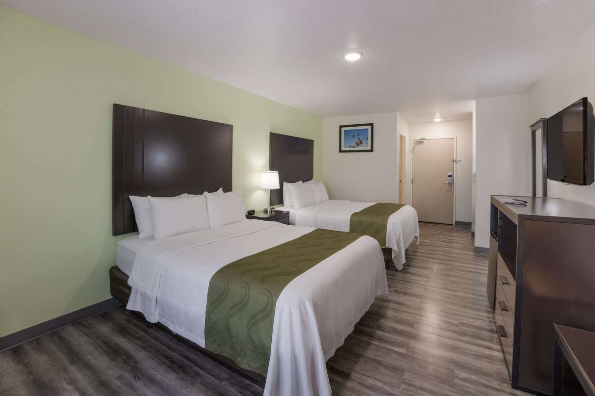 A hotel room with two beds, a desk, and a television.
