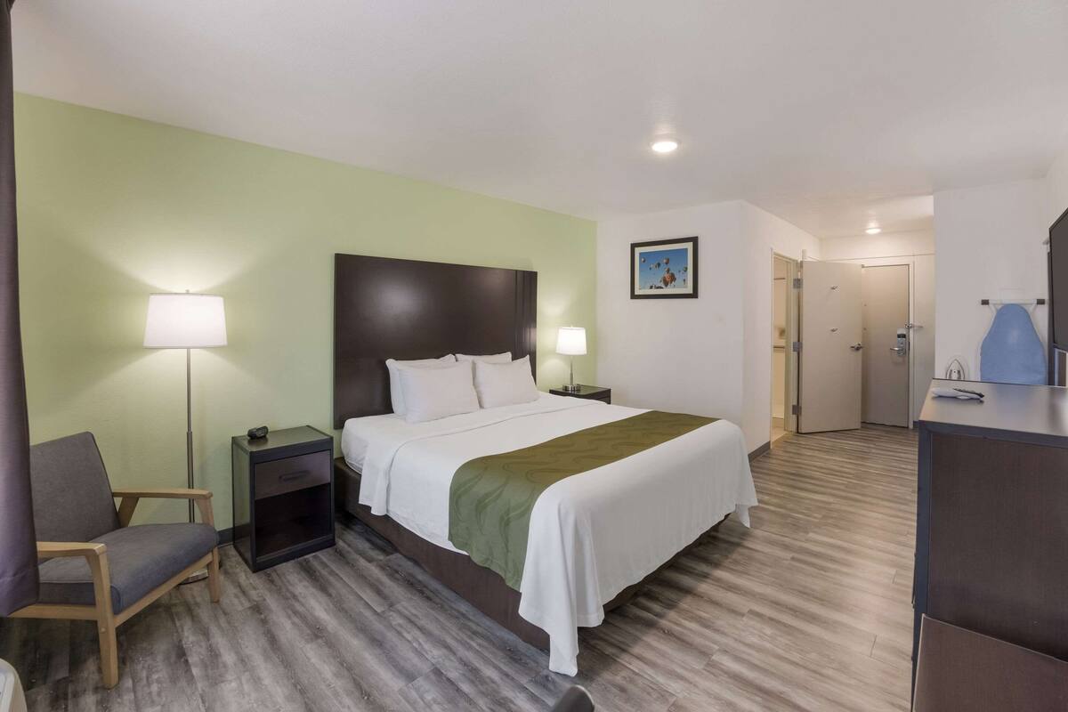 A hotel room with a bed, bedside tables, a chair, a desk, and a door.