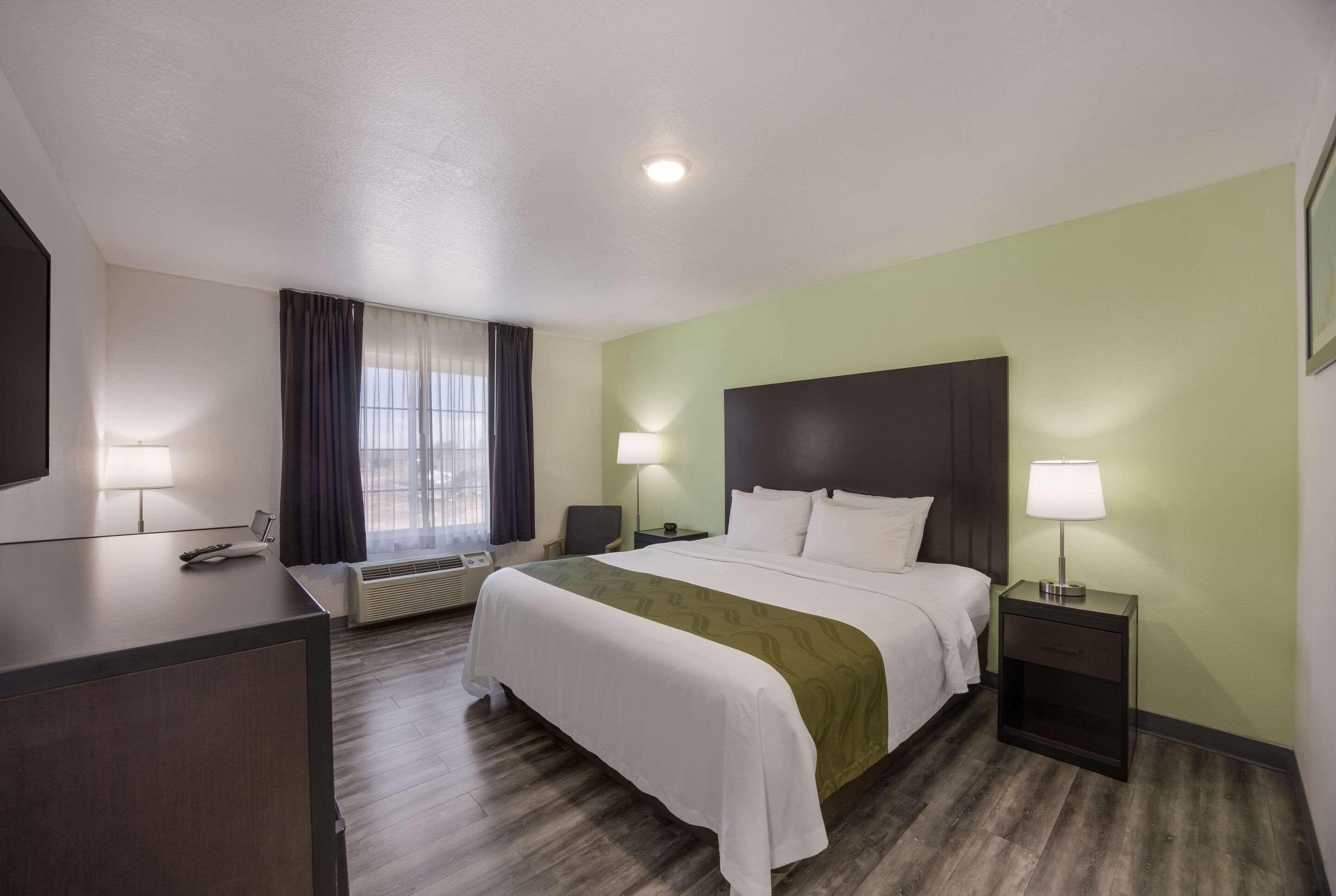 A hotel room with a bed, bedside tables, a desk, and a window with curtains.