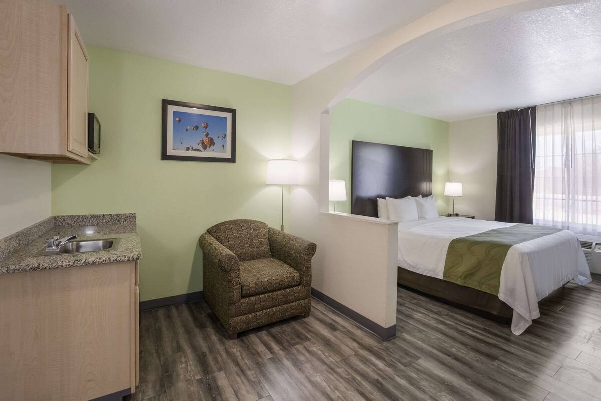 A hotel room with a bed, a chair, a desk, a sink, and a picture on the wall.