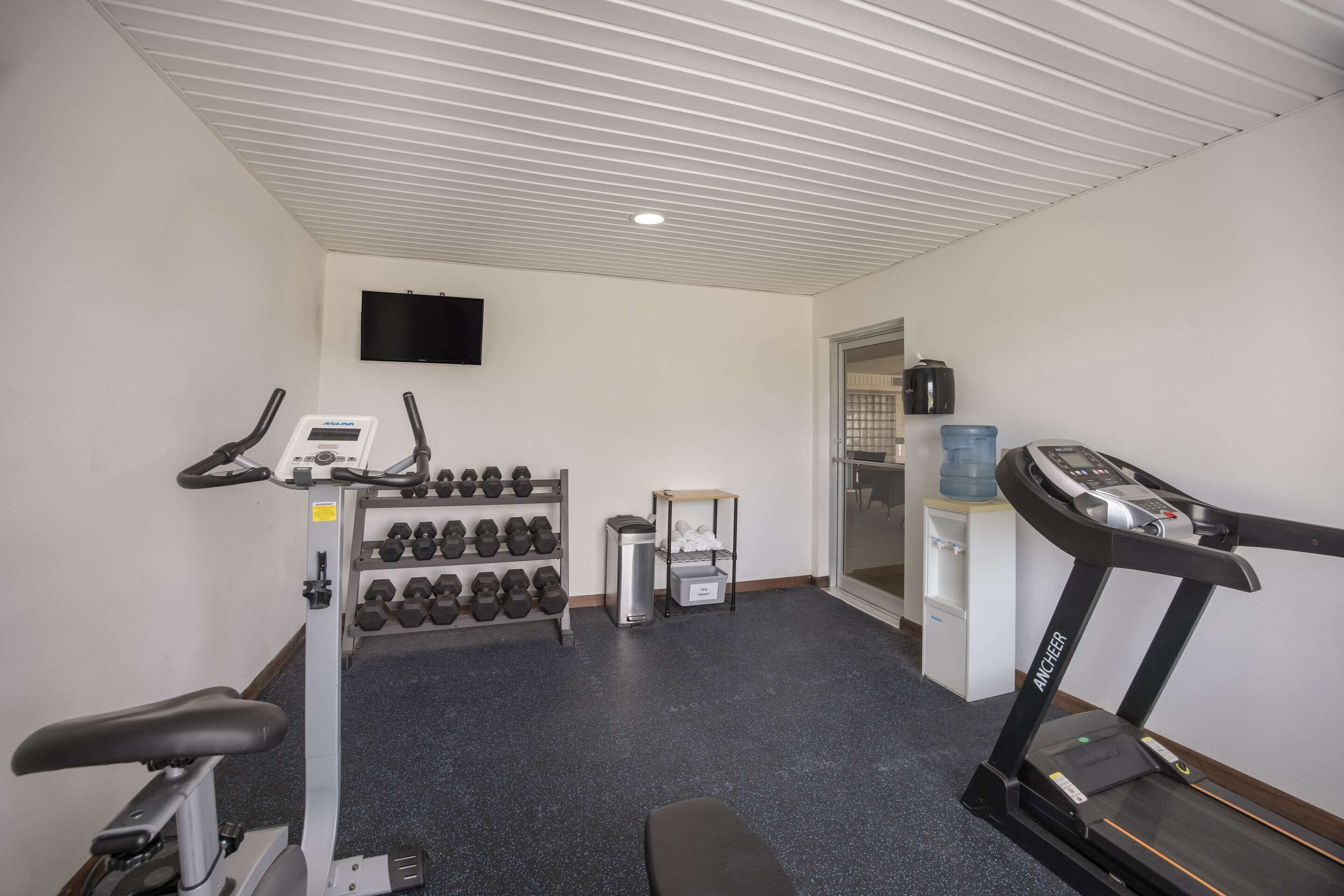 Une salle de sport équipée d’un tapis de course, d’haltères et d’un vélo d’appartement.