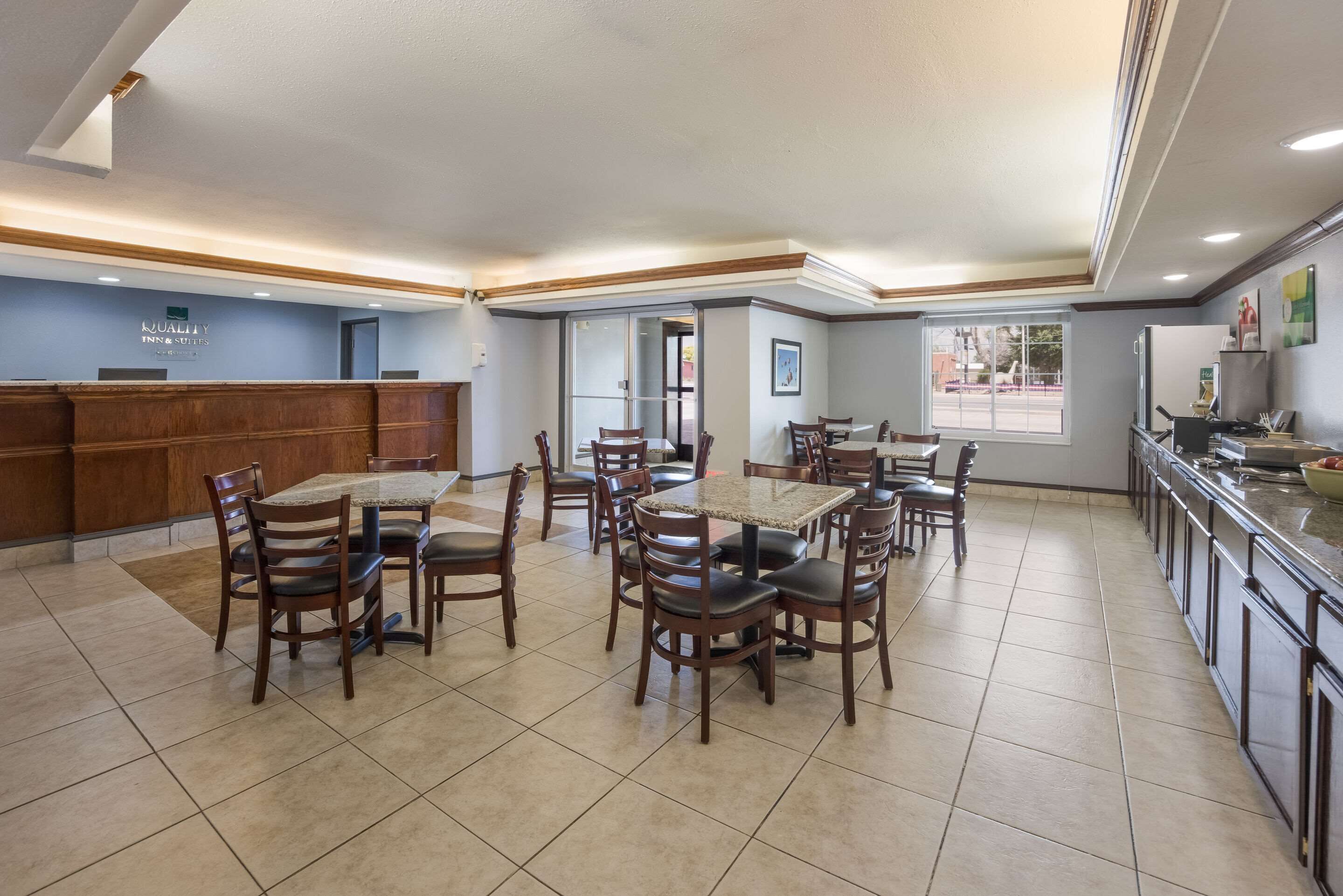 A hotel dining area with multiple tables and chairs, a reception desk, and a kitchen area.