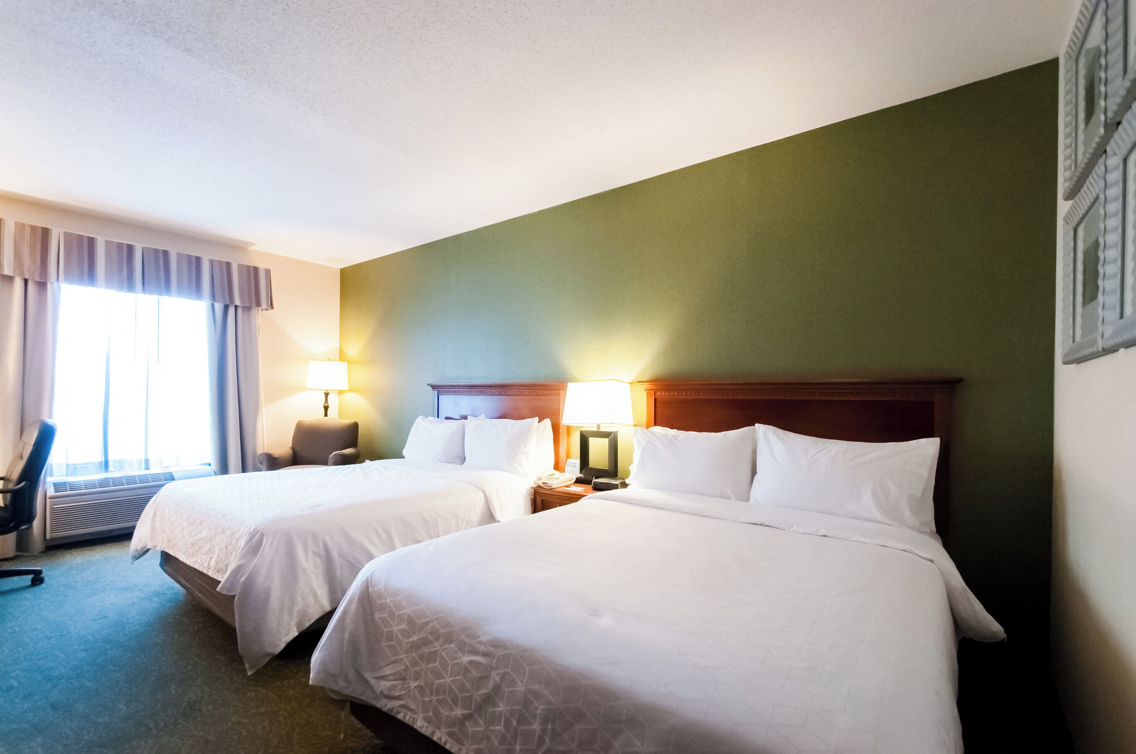 Habitación de hotel con dos camas, una silla, un escritorio y una lámpara.