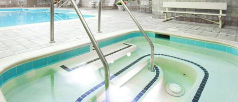 An indoor swimming pool with clear water, a diving board, and a lounge area with chairs and a bench.