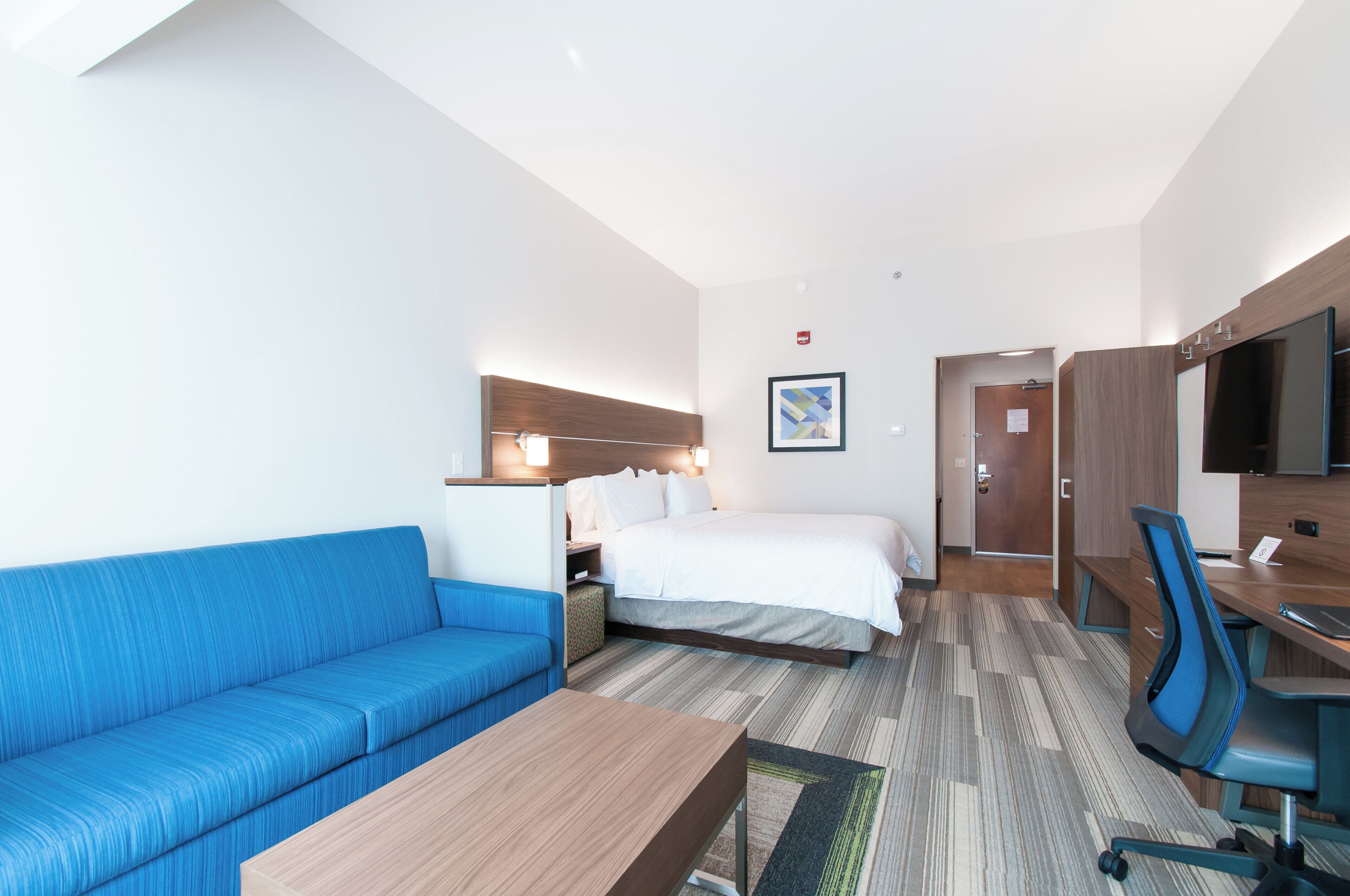 Una habitación de hotel con un sofá azul, una cama, un escritorio y un televisor.