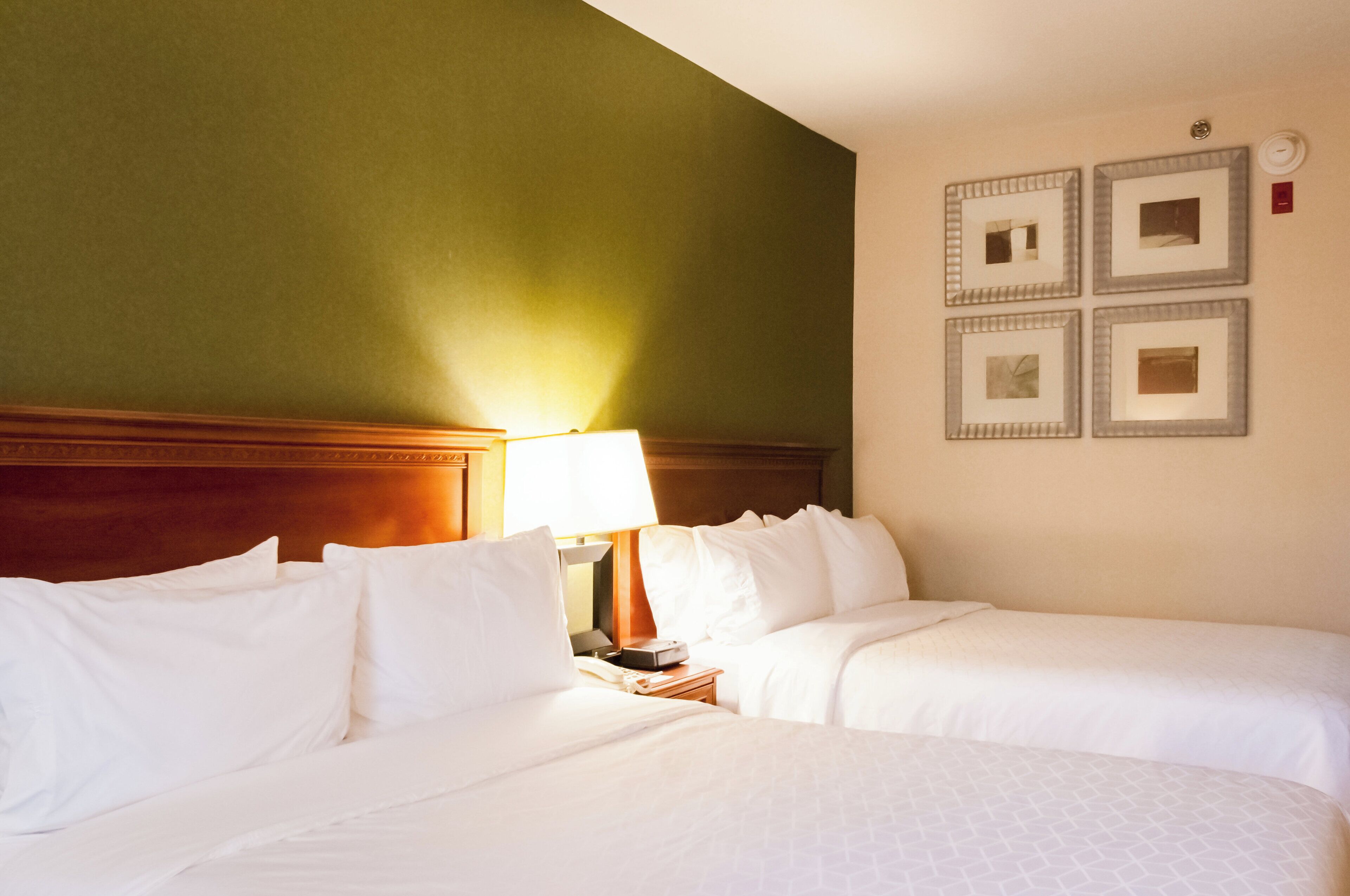 A hotel room with two beds, a nightstand, a lamp, and a wall with framed pictures.