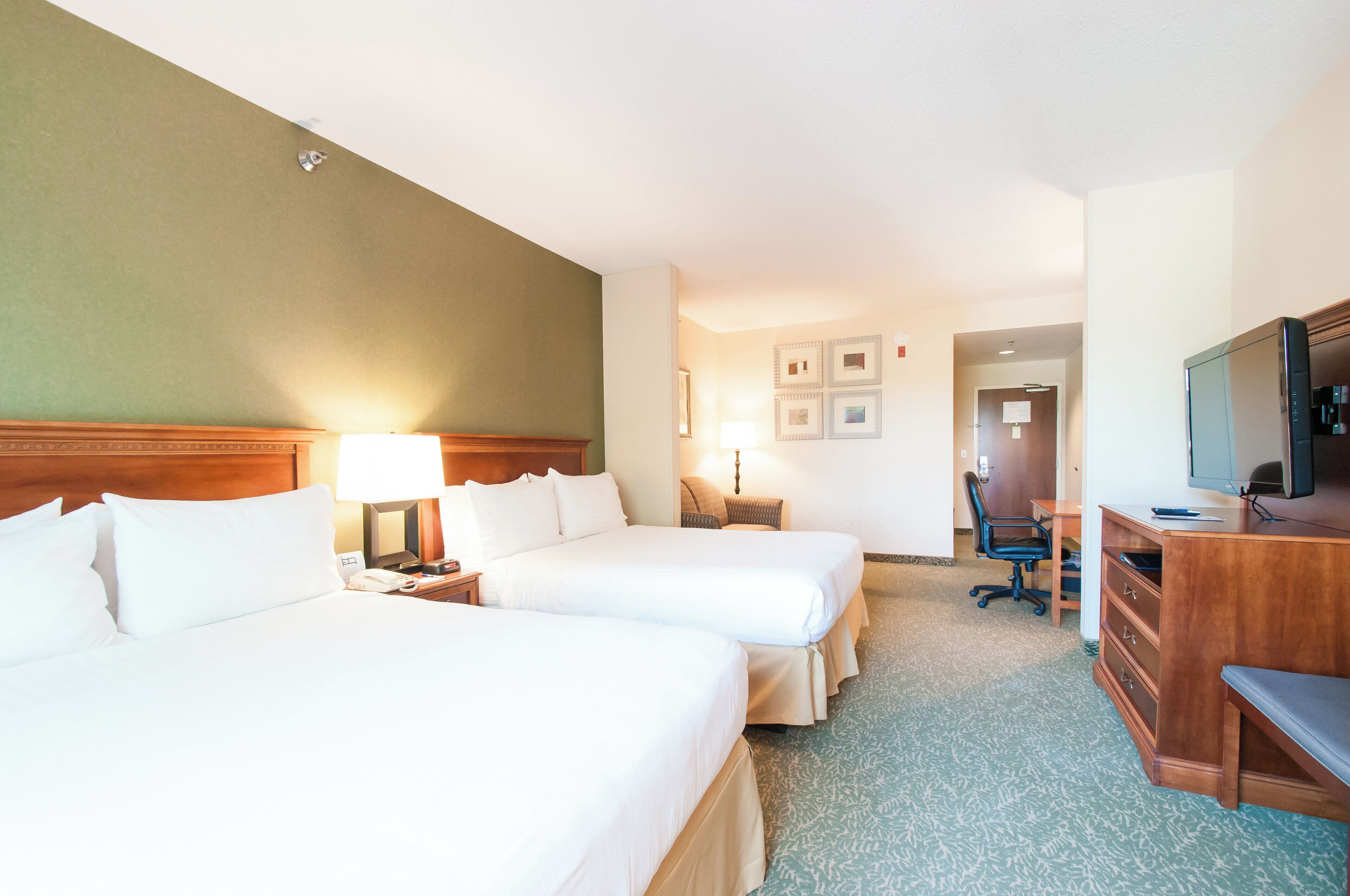A hotel room with two beds, a desk, a chair, a television, and a door leading to another room.
