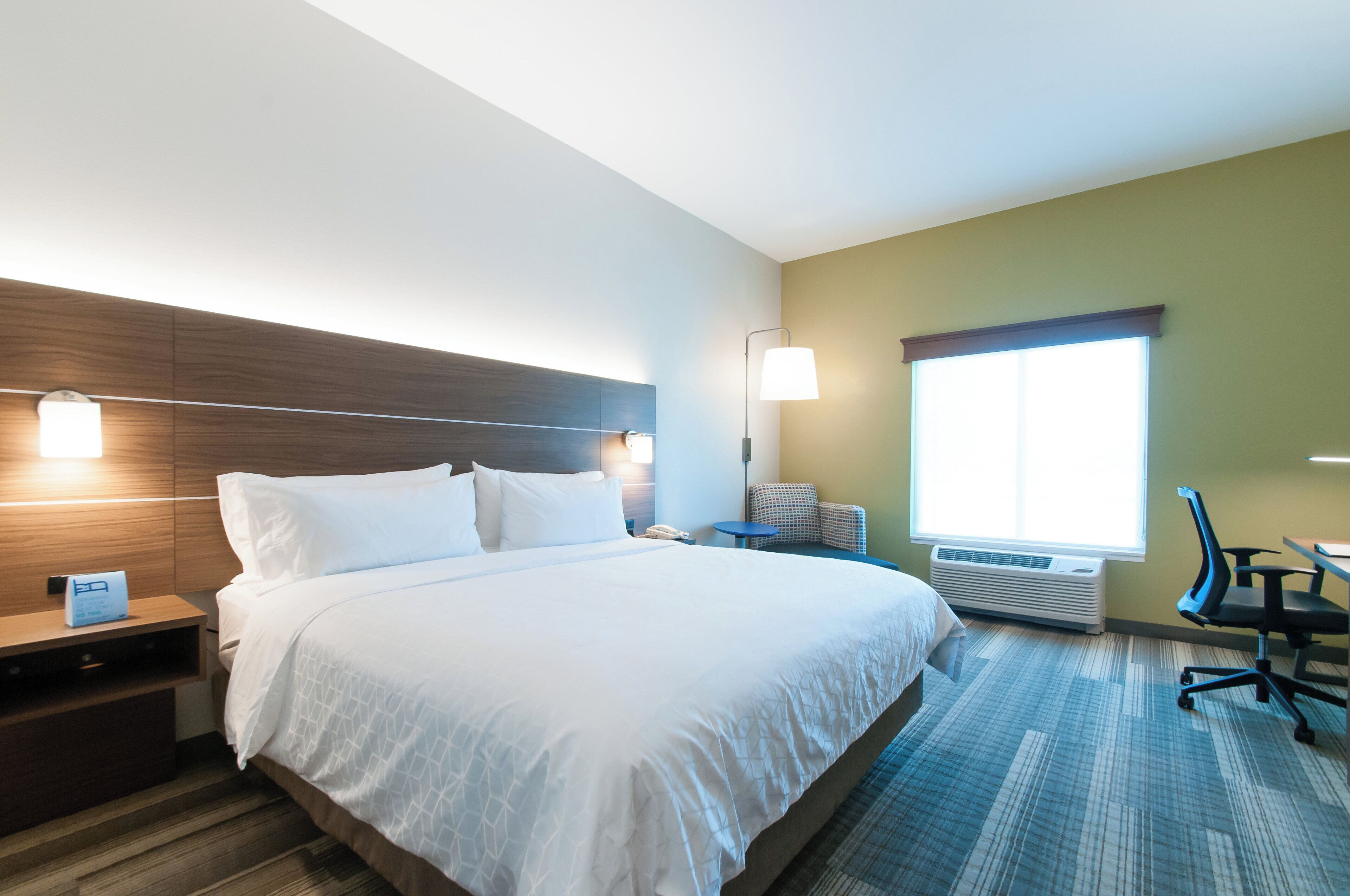 Een hotelkamer met een groot bed, een bureau, een stoel, een nachtkastje, een lamp en een raam.
