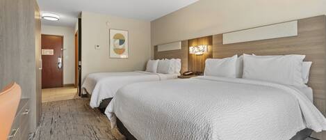 Une chambre d’hôtel avec deux lits, une tête de lit en bois, une œuvre d’art accrochée au mur et une porte donnant sur une autre pièce.