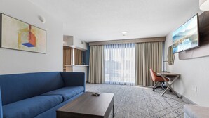 Een hotelkamer met een blauwe bank, een houten salontafel, een bureau met een oranje stoel en een grote televisie aan de muur.