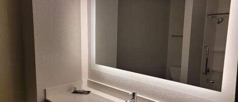 A modern bathroom with a large mirror, a sink, and a shower.
