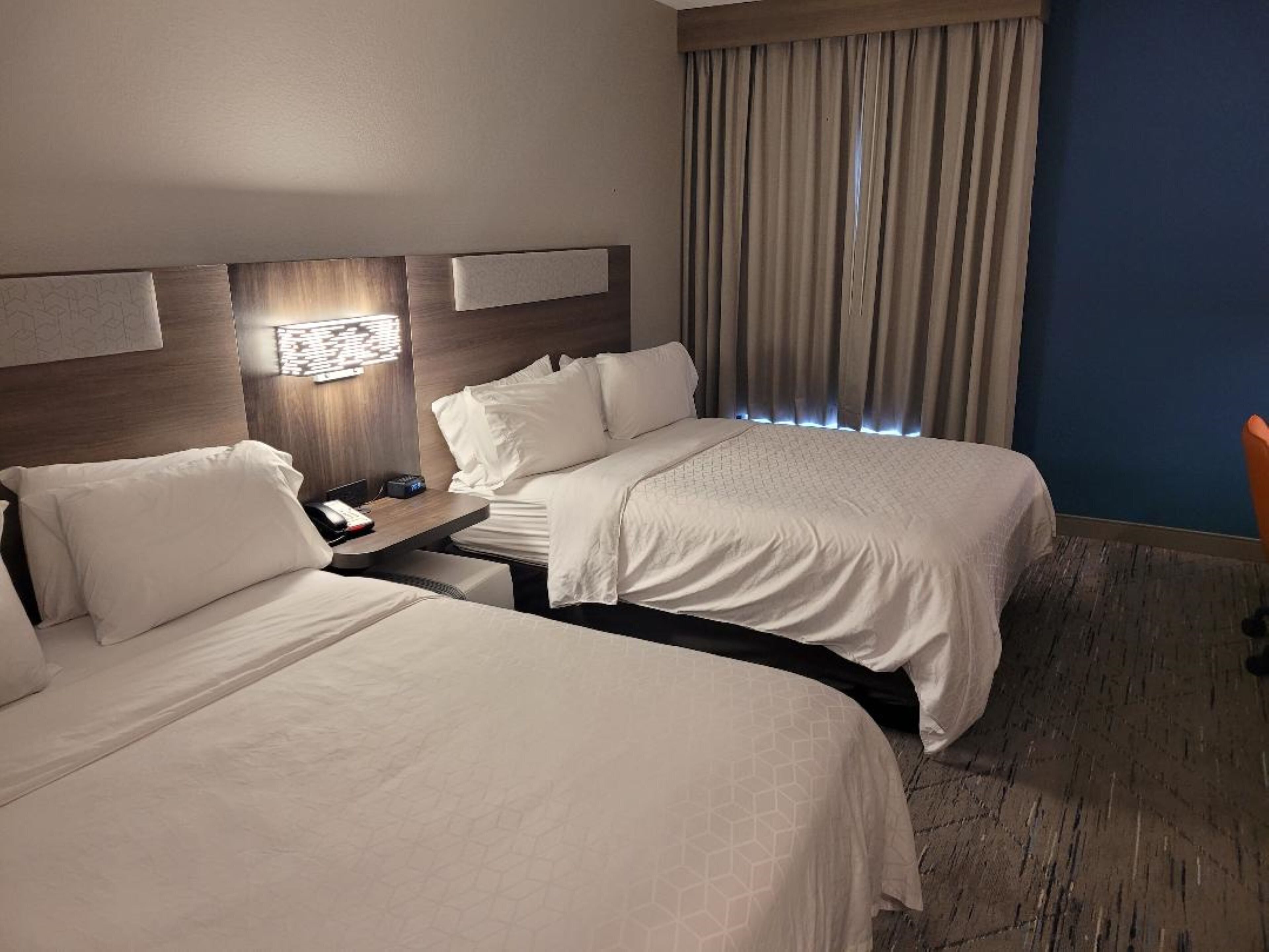 A hotel room with two beds, a nightstand, a lamp, and a window with curtains.