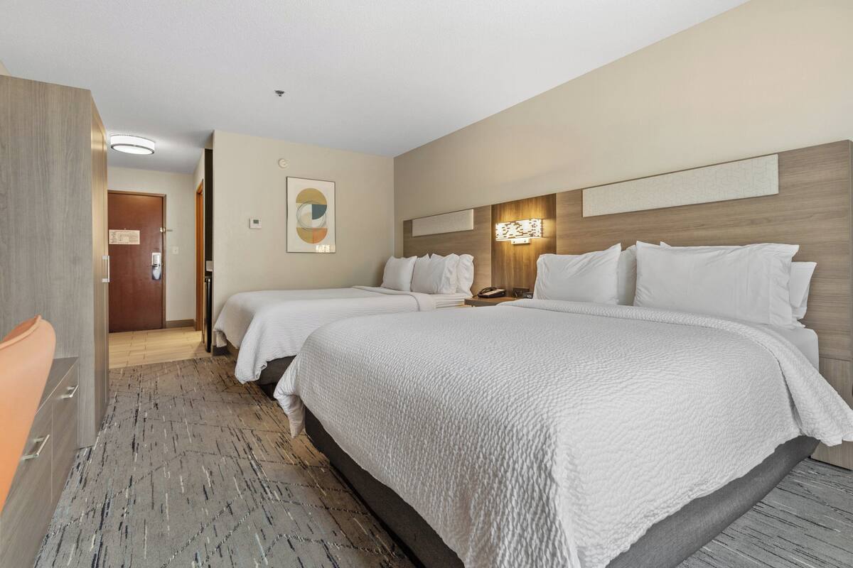 A hotel room with two beds, a wooden headboard, a wall-mounted light, and a door leading to another room.