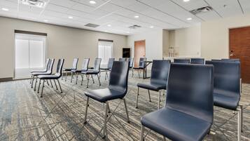 A conference room with rows of chairs, a carpeted floor, and a white ceiling with recessed lighting.