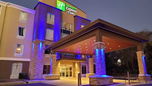 Een Holiday Inn Express & Suites gebouw met een overdekte ingang, stenen pilaren en een goed verlichte gevel.