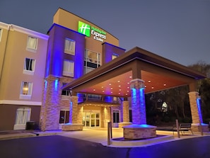 A Holiday Inn Express & Suites building with a covered entrance, stone pillars, and a well-lit facade.