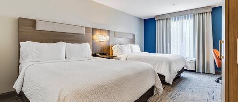 A hotel room with two beds, a nightstand, a lamp, a chair, and a large window with curtains.
