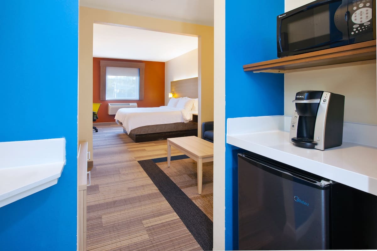 A hotel room with a bed, a desk, a microwave, and a coffee machine.