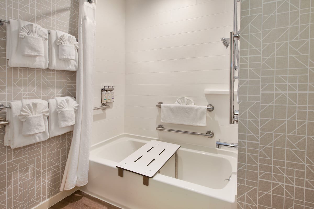 A modern bathroom with a bathtub, a shower area, and a towel rack with multiple towels.