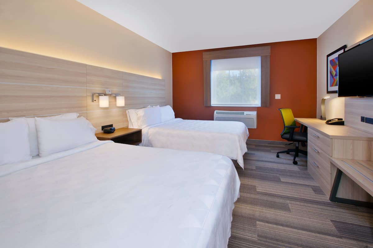 A hotel room with two beds, a desk, a chair, a TV, and a window.
