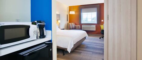A hotel room with a bed, a desk with a computer, a microwave, and a coffee maker.