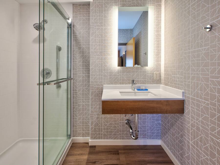 Un bany modern amb un box de dutxa de vidre, un lavabo de fusta i rajoles decorades a la paret.