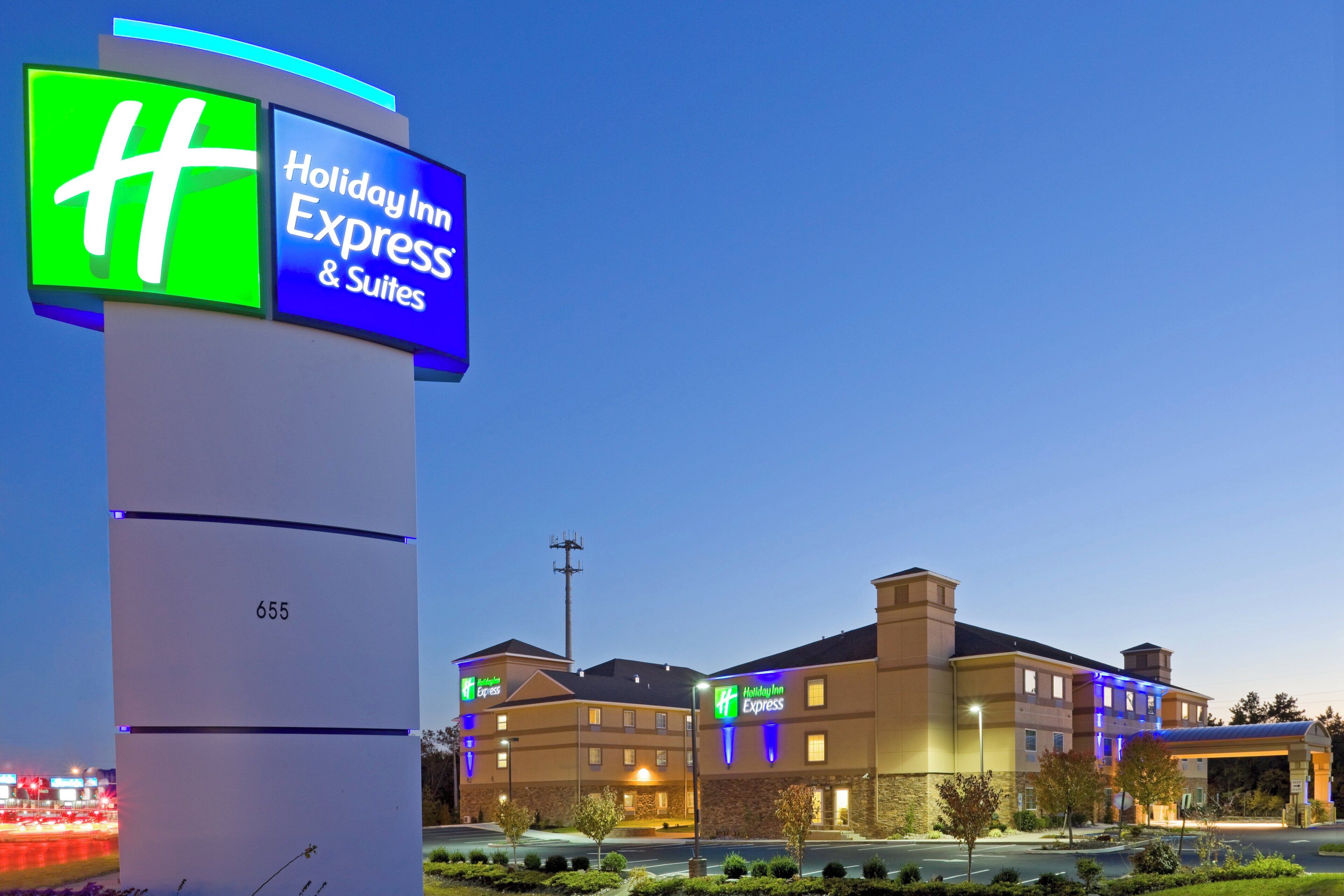 Un hotel Holiday Inn Express & Suites con un letrero llamativo, una fachada bien iluminada y una vista despejada del estacionamiento.