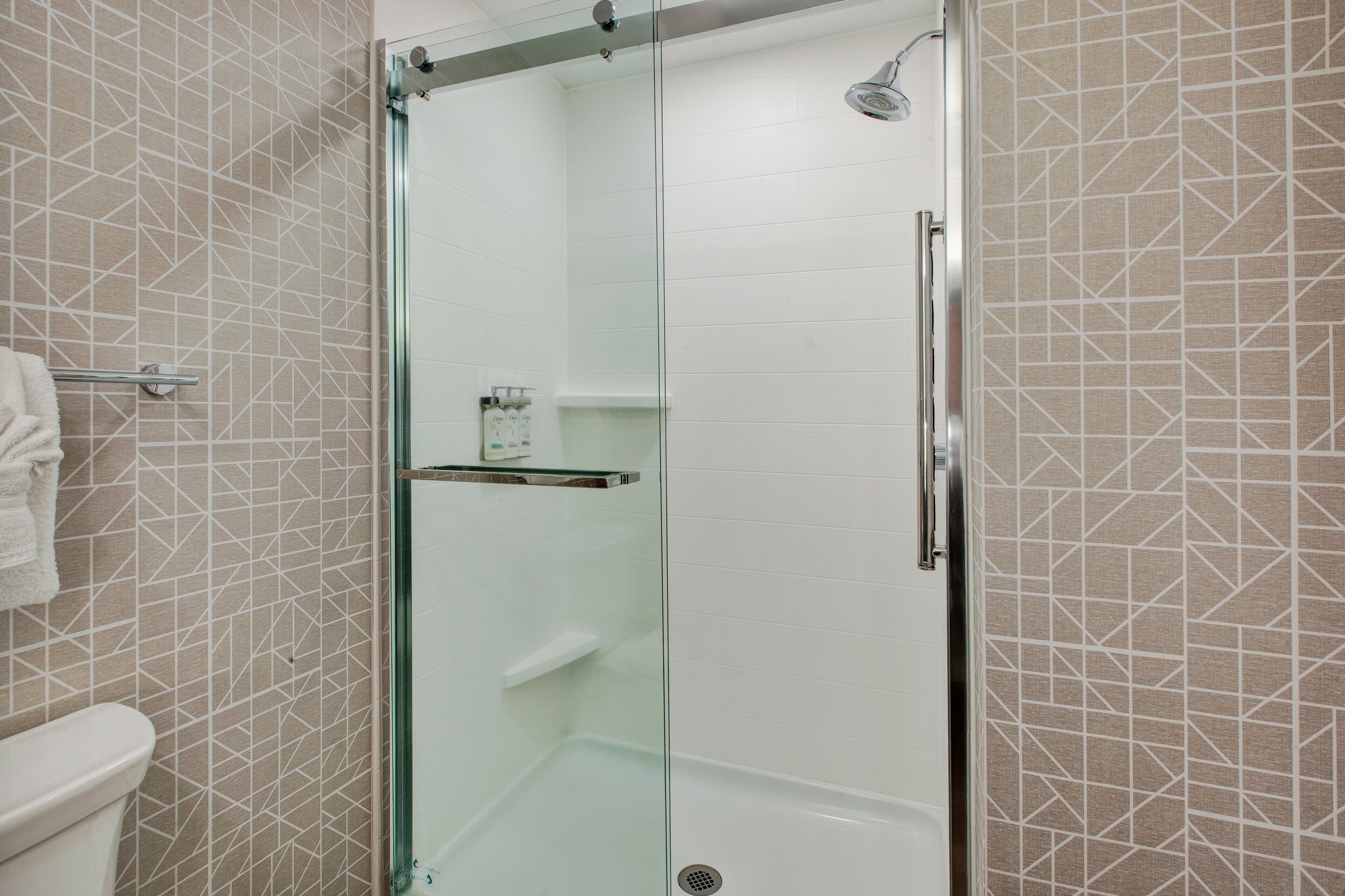 A glass-enclosed shower stall with a white tiled wall and a geometric pattern.
