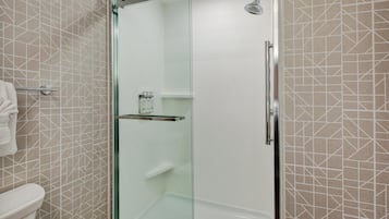 A glass-enclosed shower stall with a white tiled wall and a geometric pattern.