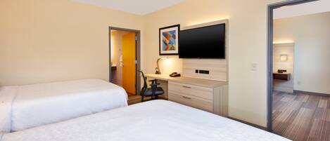 A hotel room with two beds, a desk, a flat-screen TV, and a painting on the wall.
