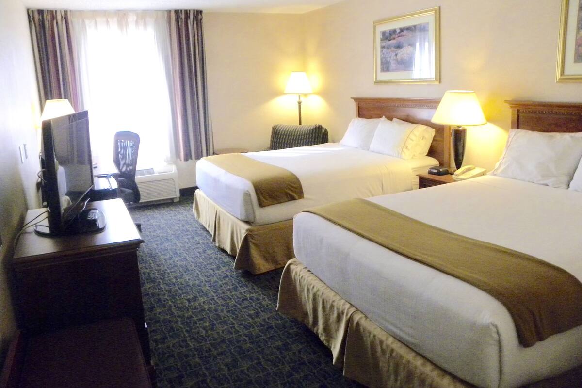 Une chambre d’hôtel avec deux lits, un bureau avec un ordinateur et deux lampes de chevet.