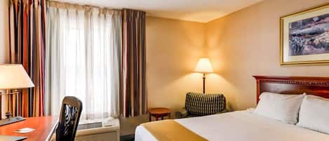 A hotel room with a bed, a desk with a chair, a lamp, and a painting on the wall.