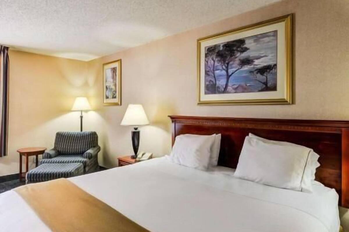Ein Hotelzimmer mit einem großen Bett, zwei Nachttischen, einem Sessel und einem Gemälde an der Wand.
