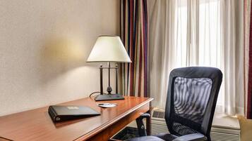 A hotel room with a wooden desk, a black office chair, a lamp, and a window with striped curtains.