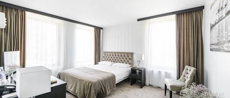 Una habitación de hotel con cama, mesita de noche, lámpara, silla y un florero con flores.