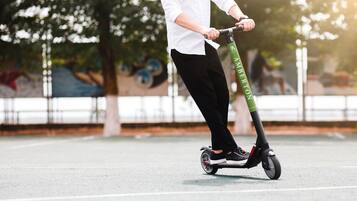 A person riding a green and black electric scooter on a paved surface.